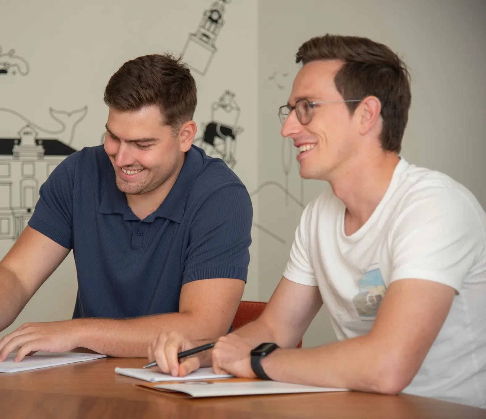 Twee collega's lachen tijdens een overleg aan tafel