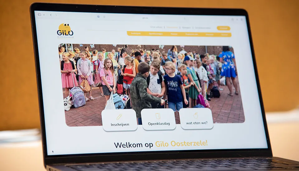 De nieuwe website van Gilo Oosterzele op een laptop, met een foto van leerlingen op de speelplaats