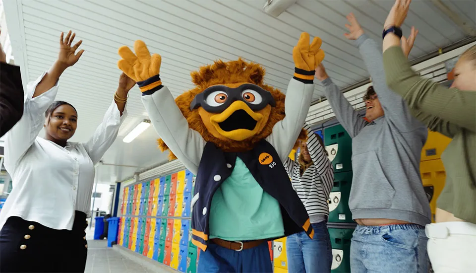 Leerlingen en leerkrachten van SJO juichen met de schoolmascotte in de gang met kleurrijke lockers